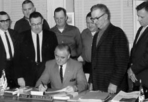 00-00-0000 Man signing document while seven men observe. Photo by Robert Mills