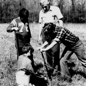 00-00-0000 Three boys plant pine seedling while adult looks on. Photo by Robert Mills