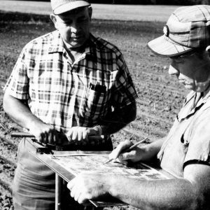 00-00-0000 Two men with clipboard standing in field.Photo by Robert Mills