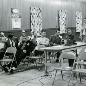 02-00-1961 Man at slide projector speaking with group of men#1-Website