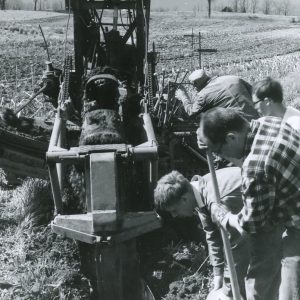 Four men gathered beside ditch digger. Photo by Robert Mills