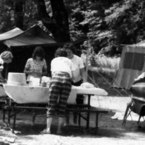 Four women at table in front of tents at campground .Photo by Robert Mills