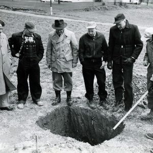 Land Judging. 7 men peering into a hole-Website