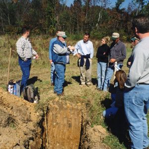 Land Judging. Group of men & women standing around hole-Website