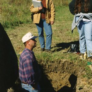 Land Judging. Man in hole as two women observe-Website