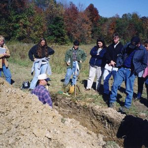 Land Judging. Man in trench. Group of men & women observing-Website