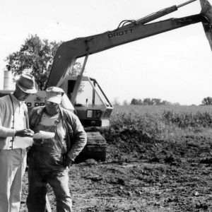 Two men examining plans with a back hoe behind them .Photo by Robert Mills