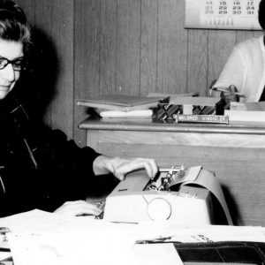 Two women-one at typewriter, one writing. Photo by Robert Mills