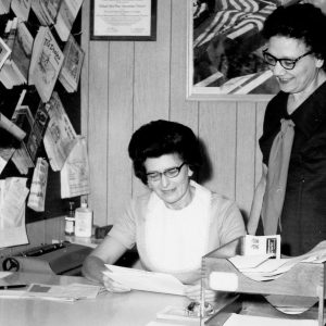 Woman sitting at desk looking at a paper while a woman standing looks on-0002.Photo by Robert Mills