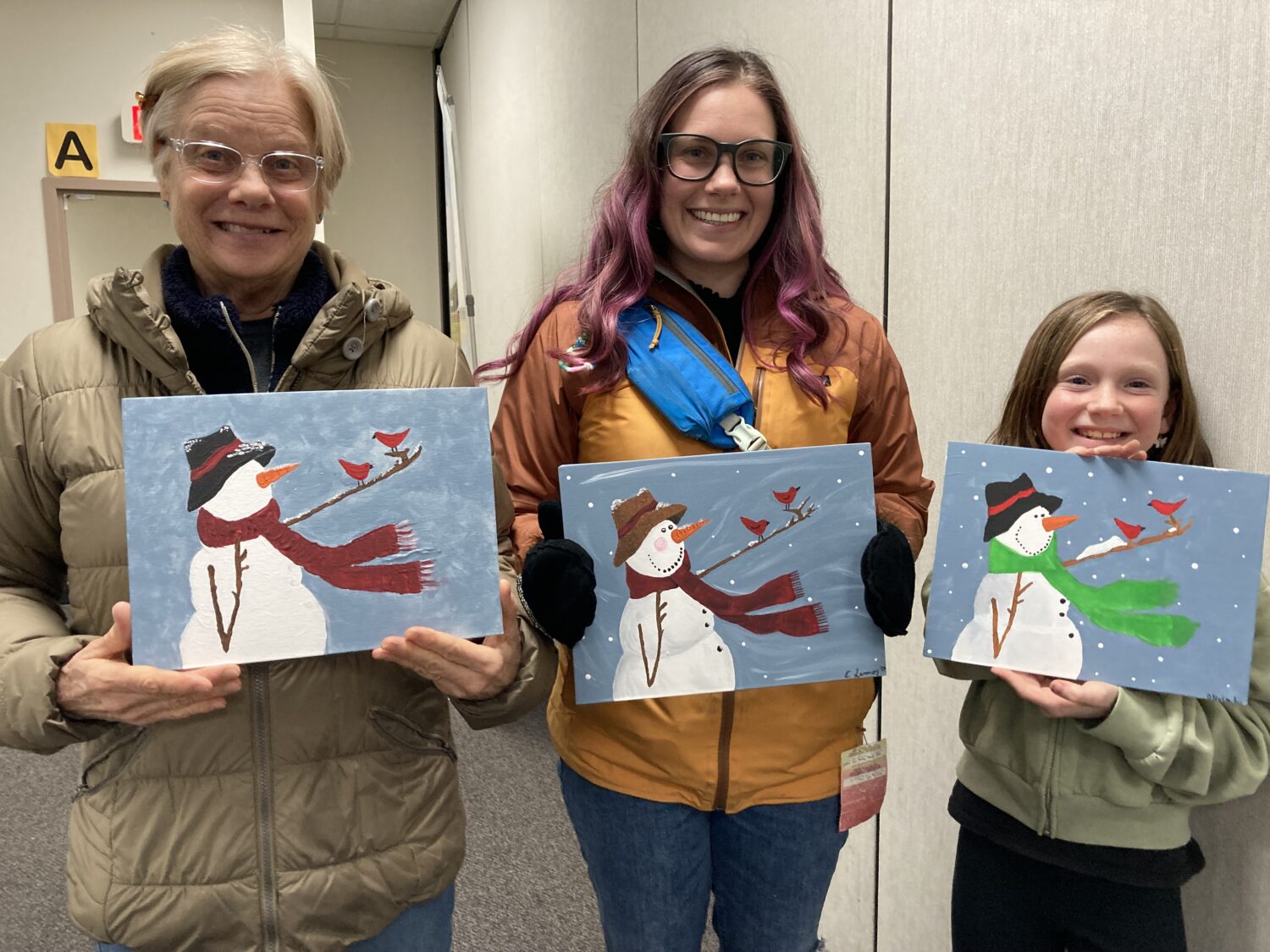 two women and a young girl holding paintings of snowmen and smiling at the camera 