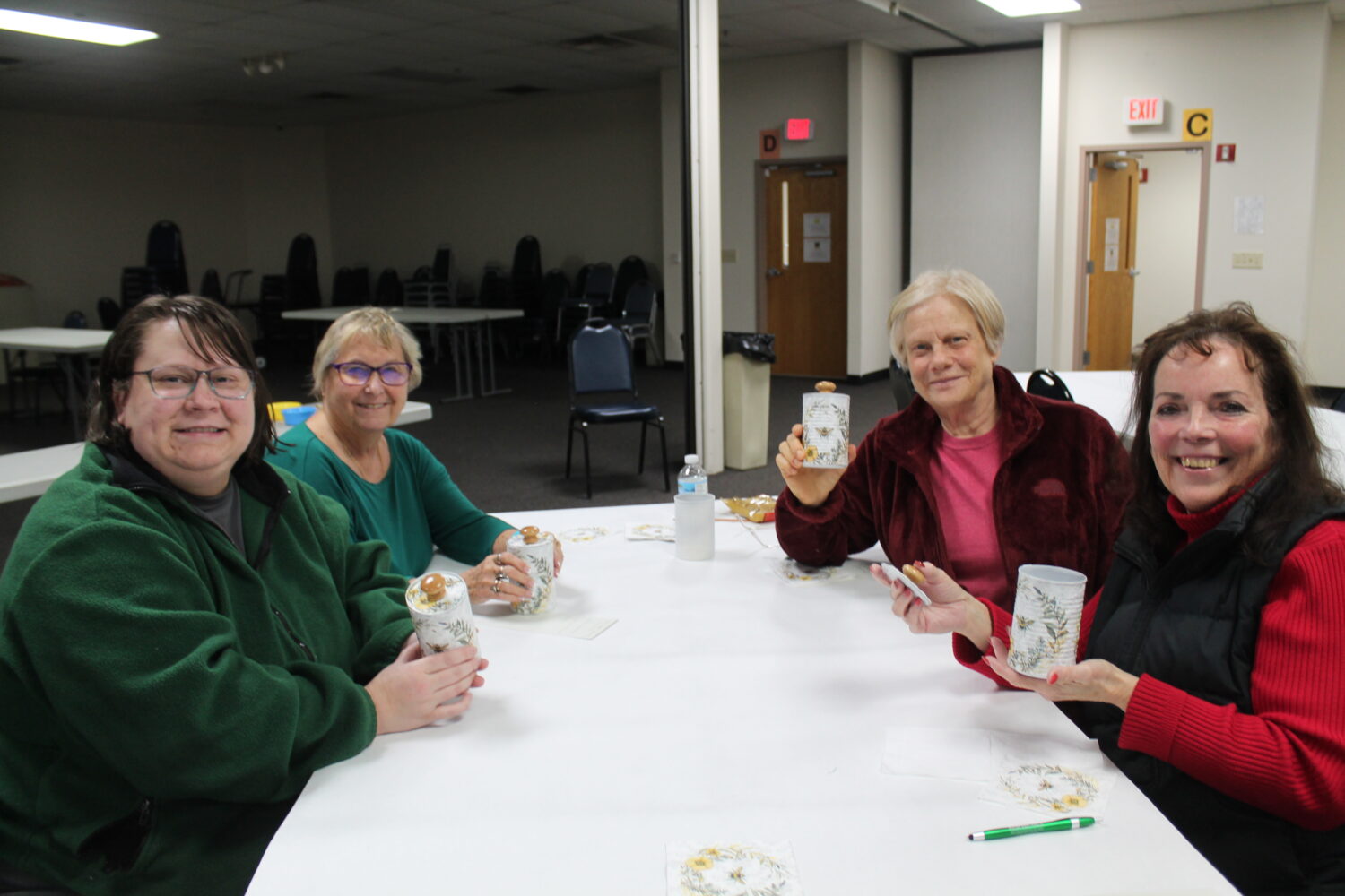 4 women gathered around a table with their recycled containers smiling for the camera. 
