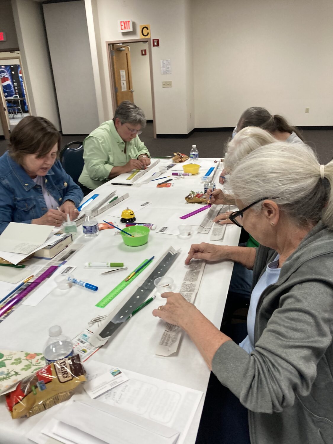 5 ladies gathered around a table making seed tape out of newspaper