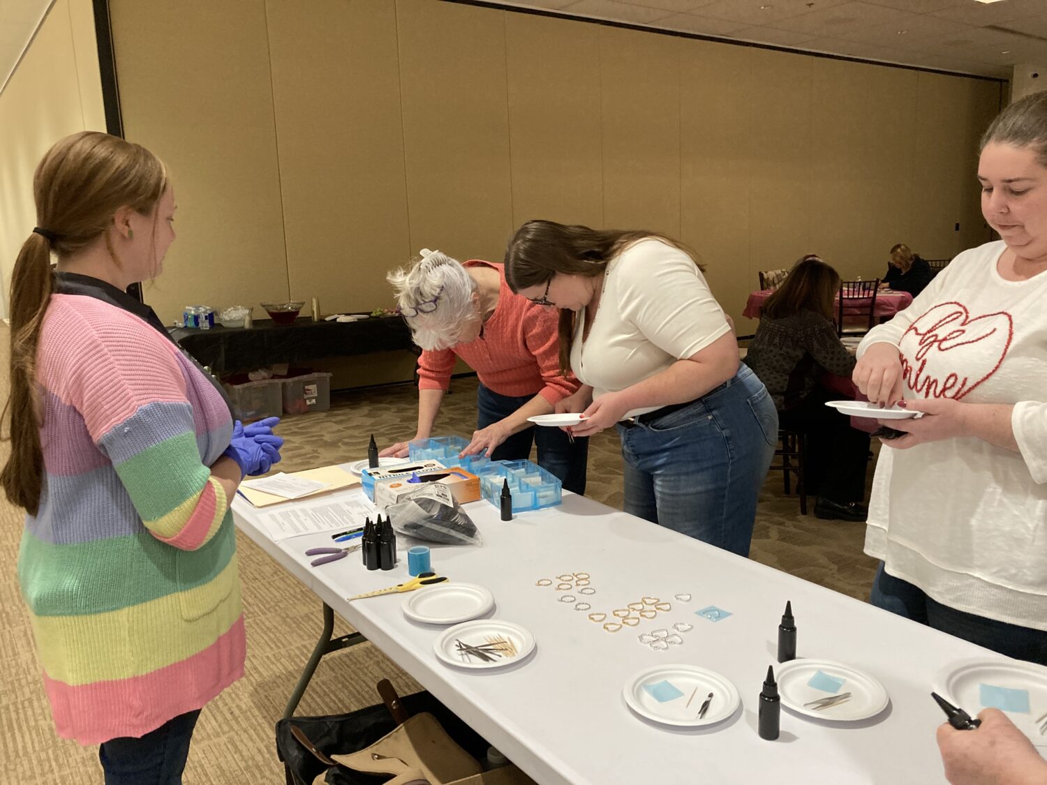 4 attendees around a table gathering supplies to make their pendants. 