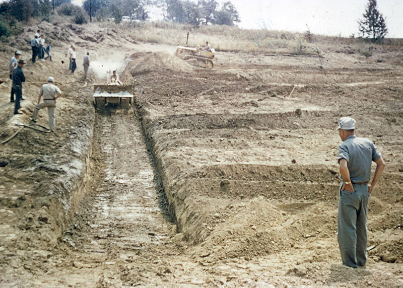 Two Pieces of Equipment Moving Soil in a Field While Several Men Observe
Photo ID#: A1021