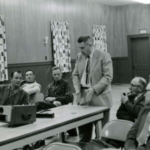 02_00_1961_Man_at_slide_projector_speaking_with_group_of_men_2_Website-5813