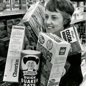 12_29_1969_Mrs._William_Zacarias_loads_arms_with_cereal_boxes_trying_to_figure_out_which_of_the_33_sizes_now_avilable_gives_her_the_most_cereal_for_her_dollar_website-2667
