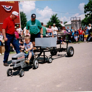 Little_boy_on_small_tractor_as_2_men_observe._Spectators_in_background_website-2383